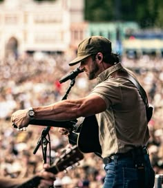 a man holding a guitar and singing into a microphone in front of a large crowd