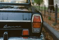 an old black car parked on the side of the road in front of a tree