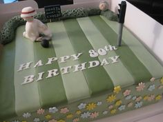 a green birthday cake with white frosting and flowers on the top, sitting in front of a sign that says happy 80th birthday