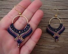 a hand holding a pair of beaded earrings on top of a piece of wood