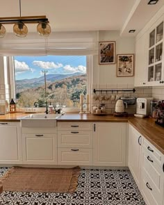 a kitchen with white cabinets and wooden counter tops next to a window overlooking the mountains