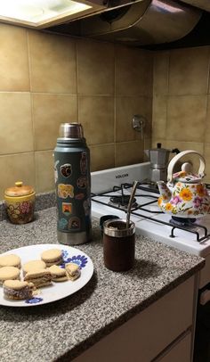 cookies on a plate next to a tea pot and stove top oven with a canister in the background