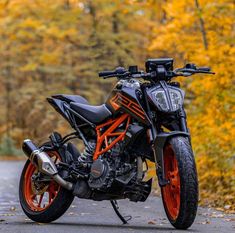 an orange and black motorcycle parked on the side of a road in front of trees