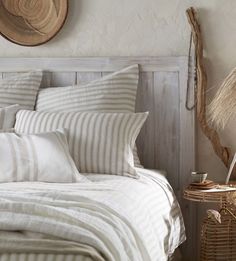 a bed with white and grey striped pillows on top of it next to a wicker basket