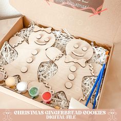 a box filled with christmas gingerbread cookies next to some paint and pencils on the table