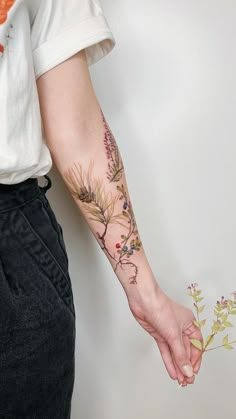 a person with a tattoo on their arm holding a flower in one hand and a plant in the other