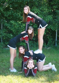 four cheerleaders posing for a photo in the grass with their arms around each other