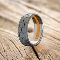 a wedding ring with an orange line in the center on top of a wooden surface