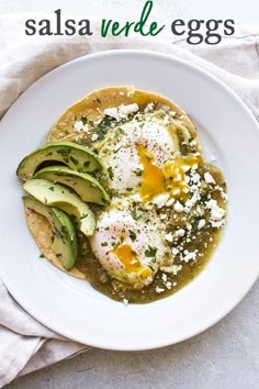 a white plate topped with eggs and avocado on top of a table next to a napkin