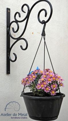 a potted plant hanging from a metal hook on a wall with flowers in it