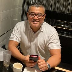 a man sitting at a table with a cell phone in his hand and a cup of coffee