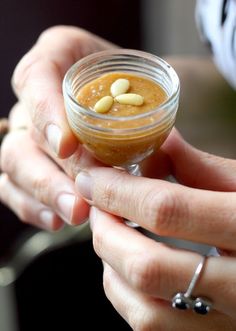 a person holding a small glass jar with food in it's hand and some nuts on top