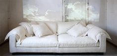 a white couch sitting in front of a wall with clouds painted on it's walls