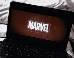 a laptop computer sitting on top of a bed with the word marvel written on it