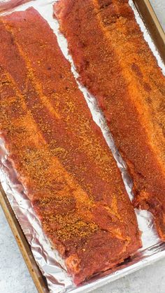 two strips of meat sitting on top of tin foil covered in seasoning next to a knife