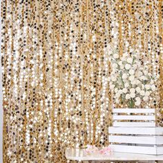 a white bench sitting in front of a window covered in gold sequins and flowers