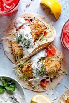 two fish tacos with sour cream sauce and garnished with lemon wedges