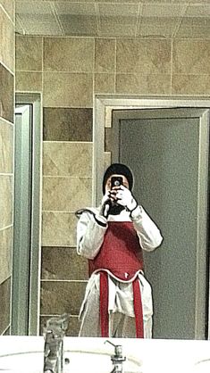 a man taking a selfie in front of a bathroom mirror while wearing an apron