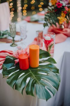 the table is set with candles and tropical leaves for an exotic touch to the centerpieces