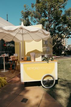 a yellow and white food cart sitting in the middle of a grass covered park area