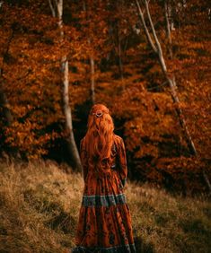 a woman with red hair is standing in the grass near some trees and looking into the distance