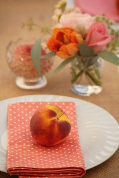 a peach sitting on top of a white plate next to a vase with flowers in it