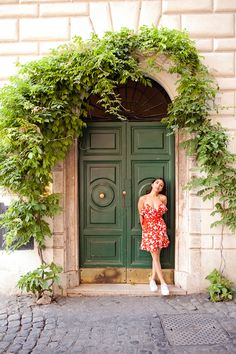 a woman standing in front of a green door with ivy growing over the top and bottom