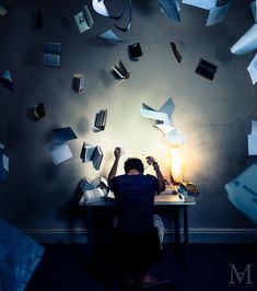 a person sitting at a desk surrounded by papers flying in the air above him and reading a book