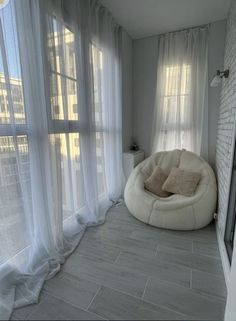 a living room with white curtains and a bean bag chair in the corner by the window