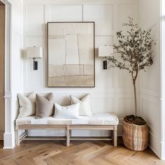 a living room with white walls and wood floors, a couch, potted plant and framed art on the wall