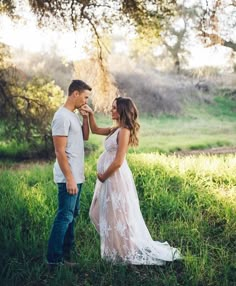 a pregnant woman standing next to a man in a field