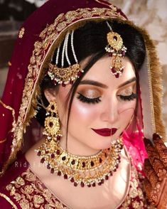 a woman in a red and gold bridal outfit with jewelry on her head, looking at the camera