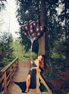 a woman sitting on a wooden bridge with balloons in the air above her head,