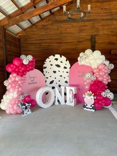 a table topped with pink and white balloons next to a sign that says, one