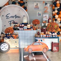 an orange car is parked in front of balloons and decorations on the wall behind it