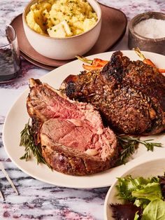 a table topped with plates of food and bowls of salad next to meat on a plate