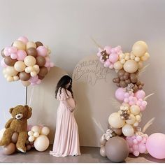 a woman standing in front of balloons and teddy bears on the floor next to a wall