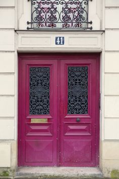 two pink doors with wrought iron bars on the top and bottom, in front of a white building