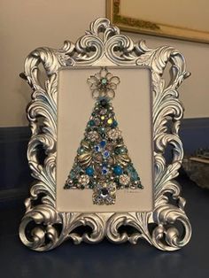 a silver frame with a christmas tree in the center and ornaments around it on a table