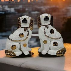 two white and gold dog figurines sitting next to each other on a ledge