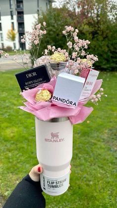 a person holding up a coffee cup filled with chocolates and flowers in the grass