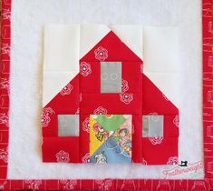 a quilted red house with white trim on the front and sides, sitting on top of a piece of fabric