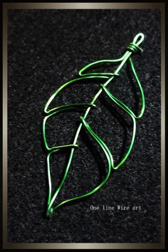 a green leaf shaped broochle sitting on top of a black surface with the words one line wire art written below it