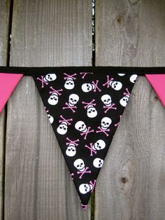 a black and pink bandana with skulls and crossbones is hanging on a wooden fence