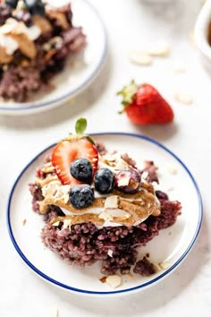 two white plates topped with blueberries and granola covered in whipped cream next to strawberries