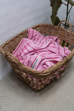 a wicker basket filled with pink towels next to a potted plant on the floor