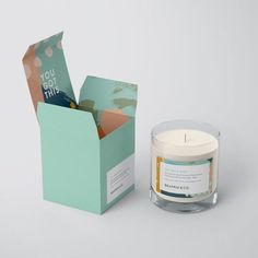 an open box next to a candle on a white surface with a card in it