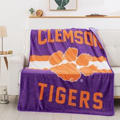 an orange and purple blanket with the word clemson on it in front of a white couch