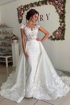 a woman in a white wedding dress standing next to a wall with flowers on it