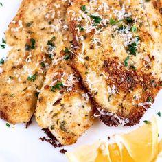 two pieces of chicken with parmesan cheese and lemon wedges on a white plate